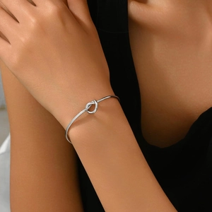Dettaglio di un bracciale a fascia aperta in argento con nodo in acciaio lucido su un polso