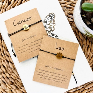 Detail of handmade Cancer and Leo zodiac charm bracelets with gold pendants on display cards