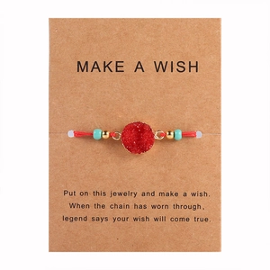 Dettaglio del braccialetto dei desideri rosso con pietra in resina su carta regalo