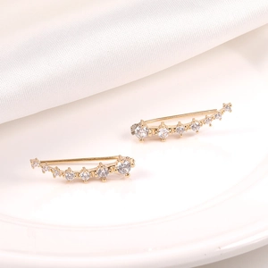 Detalle de pendientes trepadores dorados con circonitas sobre fondo de seda blanca