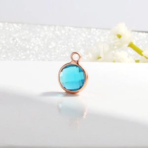 Close-up of light blue round birthstone pendant with faceted crystal and rose gold frame