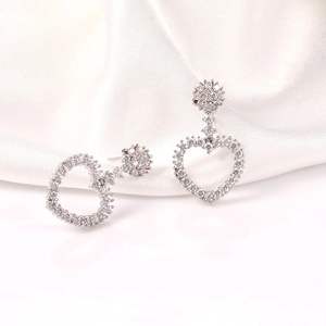 Detalle de pendientes de corazón en plata con circonitas sobre fondo de seda blanca