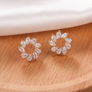 Detalle de pendientes de girasol dorados con circonitas brillantes sobre seda blanca