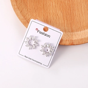 Detalle de pendientes de flor con circonitas y base plateada en tarjeta de muestra