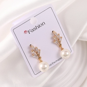 Detalle de pendientes de lujo con circonitas doradas y colgante de perla brillante