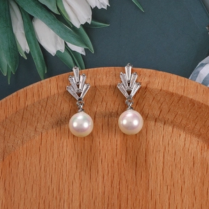 Detalle de pendientes de abanico con circonitas y perlas blancas en bandeja de madera