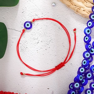 Detailopname van rood gevlochten armband met blauwe Evil Eye kraal en gouden accenten