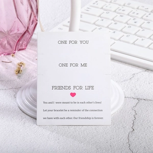 Primer plano de una tarjeta blanca para pulseras con mensaje de amistad e icono de corazón