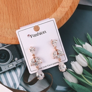 Detalle de pendientes de hoja oro rosa con gotas de circón sobre tarjeta blanca