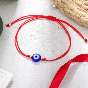 Detail van handgemaakte rode gevlochten armband met blauwe Evil Eye kraal en zilveren accenten