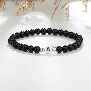 Detail van een zwarte kralenarmband met witte letter A kraal en zilveren accenten