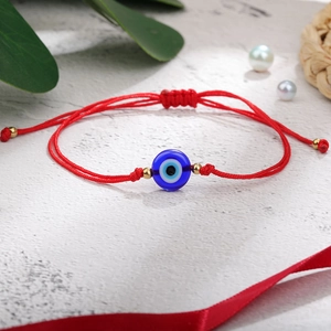 Detailweergave van een rood gevlochten Evil Eye armband met blauwe kraal op marmer