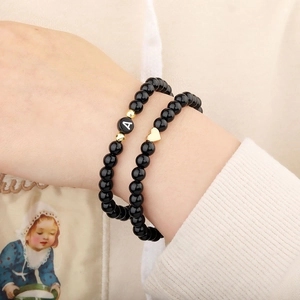 Detail van zwarte kralenarmband met letter A en goudkleurig hartje om de pols