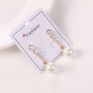 Detalle de pendientes de oro con circonitas escalonadas y grandes perlas blancas