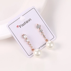 Detalle de pendientes largos dorados con circonitas claras y perlas blancas redondas