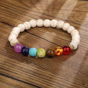 Nahaufnahme von 7 Chakra-Natursteinen und weißen Türkisperlen auf dunklem Holzgrund