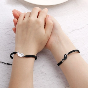 Detailansicht der gewebten Paar-Armbänder mit Yin-Yang-Anhängern auf Händen vor weißem Stein