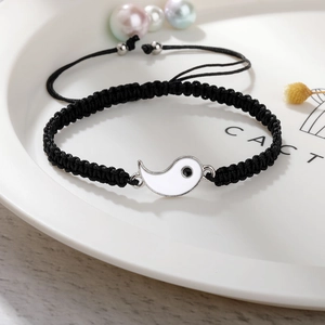 Detail eines handgewebten schwarzen Kordelarmbands mit weißem Yin-Yang-Anhänger
