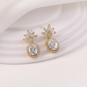 Detalle de pendientes dorados con circonitas corte marquesa y gota ovalada sobre seda blanca