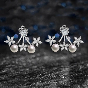 Detalle macro de pendientes de flores de circón y perlas blancas sobre fondo oscuro