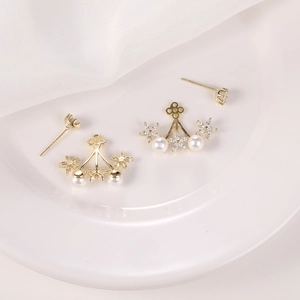 Detalle de pendientes de flores doradas con perlas blancas y circonitas brillantes