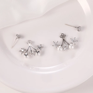 Vista macro de pendientes de flores plateados con circonitas y perlas sobre seda blanca