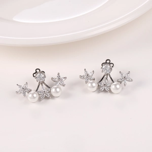 Detalle de pendientes de flores con circonitas y perlas sobre una superficie blanca