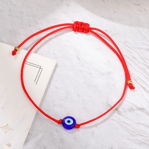 Close-up of red braided Evil Eye bracelet with blue bead and gold accents on marble background