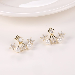 Detalle de pendientes florales dorados con cristales brillantes y perlas blancas