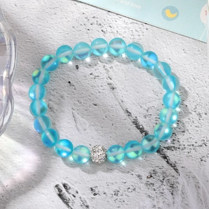 Macro detail of a beaded elastic bracelet with light blue moonstone beads and a crystal charm