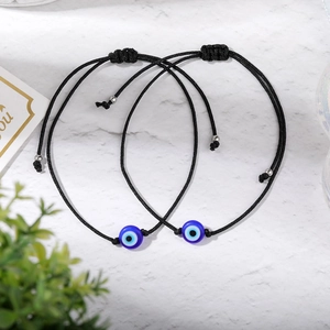 Two-piece black braided evil eye bracelets on white marble with green leaf decor