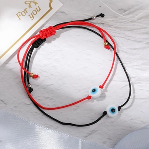 Detail view of woven Evil Eye bracelets in red and black on a white marble background
