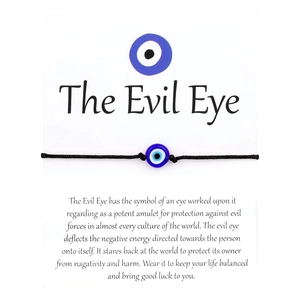 Macro shot of minimalist braided black string bracelet with blue Evil Eye bead on display card
