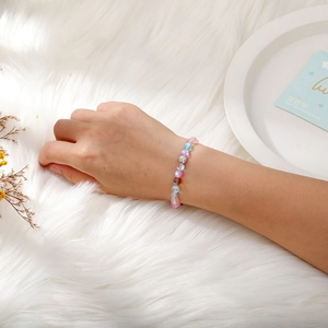 Wrist view of iridescent beaded elastic bracelet with silver crystal charm on plush fabric