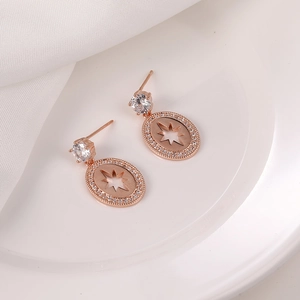 Detalle de pendientes de oro rosa con circonitas y estrella sobre un plato de cerámica
