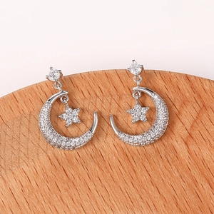 Detalle de pendientes de lujo con circonitas de luna y estrella en soporte de madera