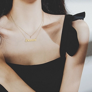 Detail of a layered gold Gemini zodiac necklace with gothic lettering on a female model