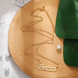 Golden Gemini zodiac necklace with stainless steel letter pendant on a wooden tray