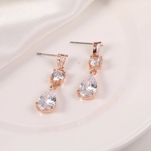Detalle macro de pendientes colgantes en oro rosa con circón sobre seda blanca fina