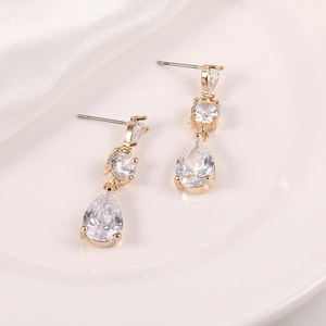 Detalle de pendientes dorados con tres circonitas y un colgante elegante en forma de pera