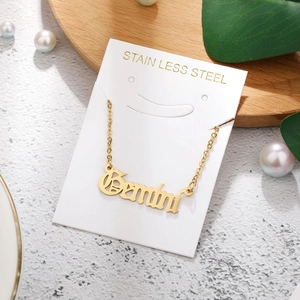 Detail of golden Gemini stainless steel gothic letter pendant on elegant white card display