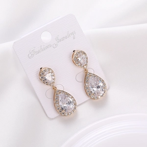 Detalle de pendientes de gota con circonitas y baño de oro sobre seda blanca