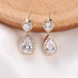 Detalle de pendientes de gota dorados con pavé de circonitas en soporte de madera