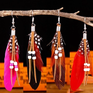 Dettaglio di orecchini bohémien con piume in quattro colori su sfondo di ramo vintage