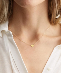 Dettaglio di una collana a cuore dorata con incisione della lettera M su catena fine