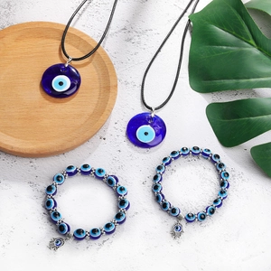Detailed view of evil eye necklaces and hamsa hand beaded bracelets on a stone background