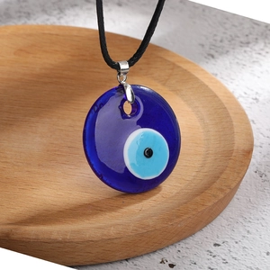 Detailed macro shot of the deep blue glass Evil Eye pendant with black cord on wood