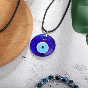 Detail view of Evil Eye pendant necklace and beaded bracelet set on textured background