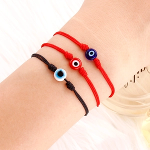 Nahaufnahme von drei Evil-Eye-Armbändern aus geflochtenem Seil in Rot und Schwarz am Handgelenk