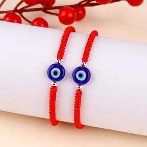 Pair of red woven Evil Eye bracelets on display with decorative red berry branch